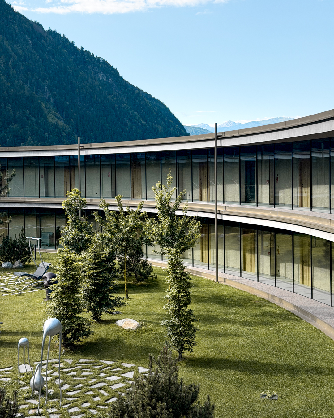 Eco aparthotel alpino con architettura sostenibile e forma circolare integrata nel prato, esempio di progettazione integrata a basso impatto ambientale